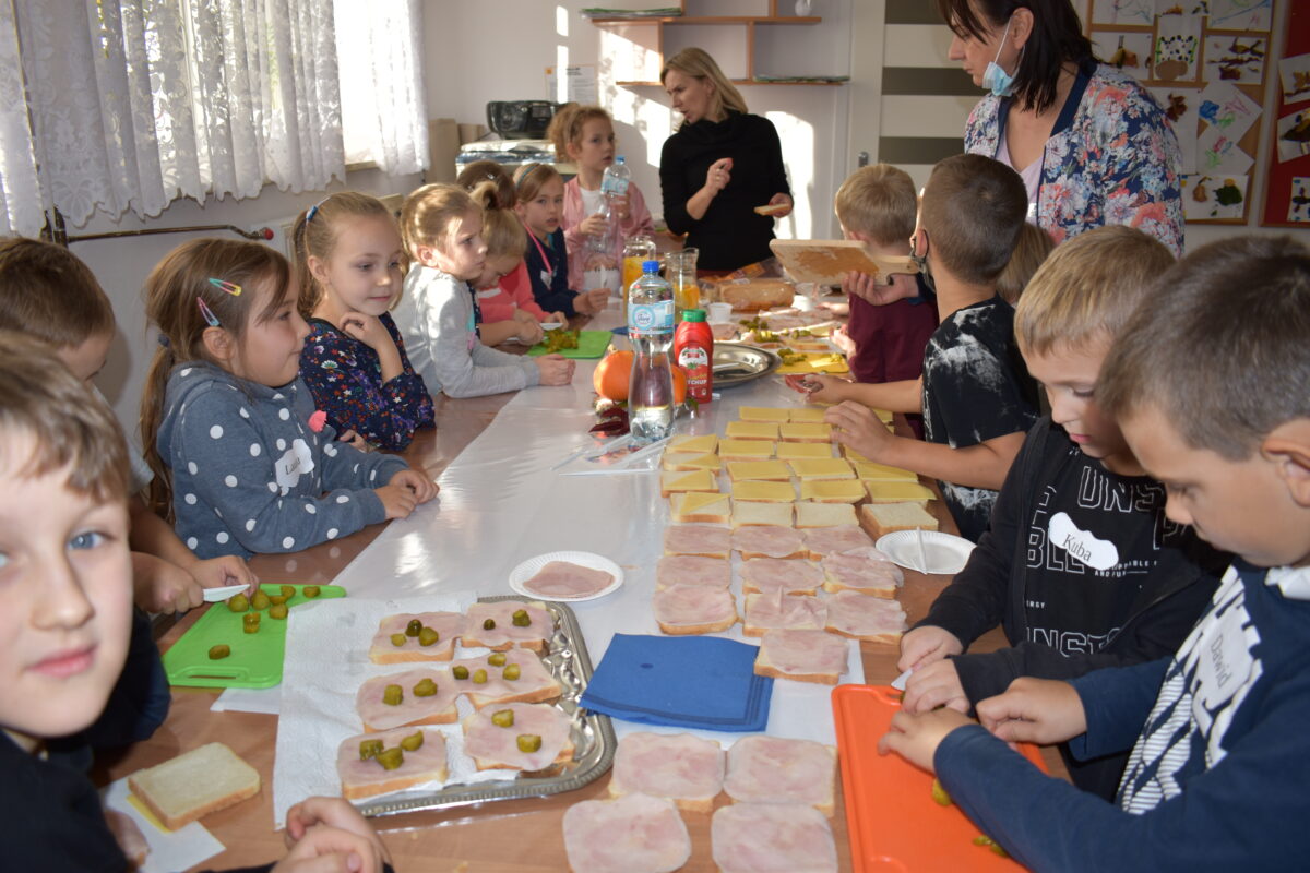 Grupa dzieci przygotowuje kanapki, na stole jest wędlina i ser, chłopcy kroją ogórki.