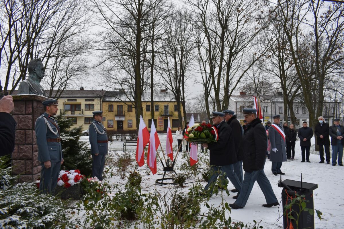 Trzej mężczyźni składający kwiaty przed pomnikiem.