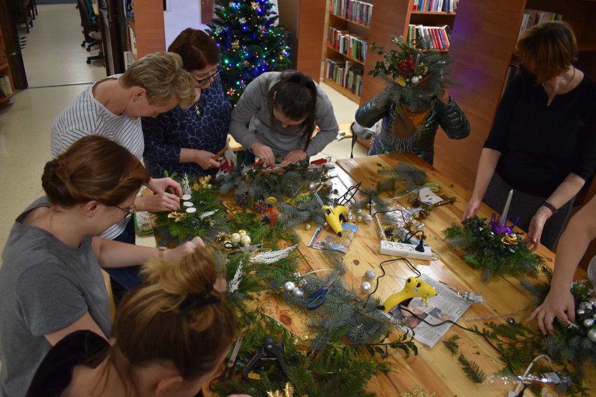 W bibliotece przy dużym stole kobiety robią stroiki, leżą już na nim w części zrobione stroiki
