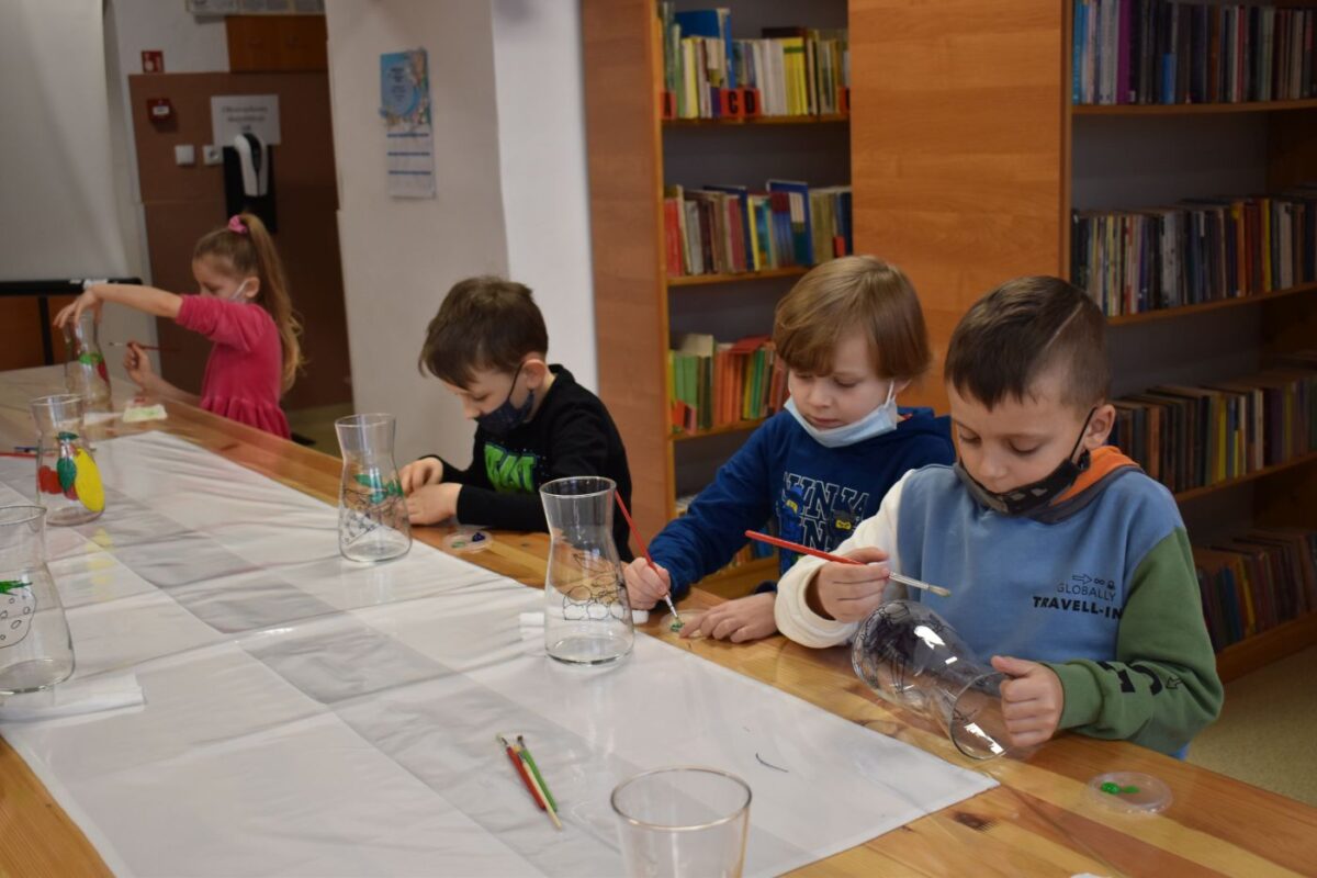 W bibliotece grupka dzieci z kolorowymi noskami za nimi regały z książkami