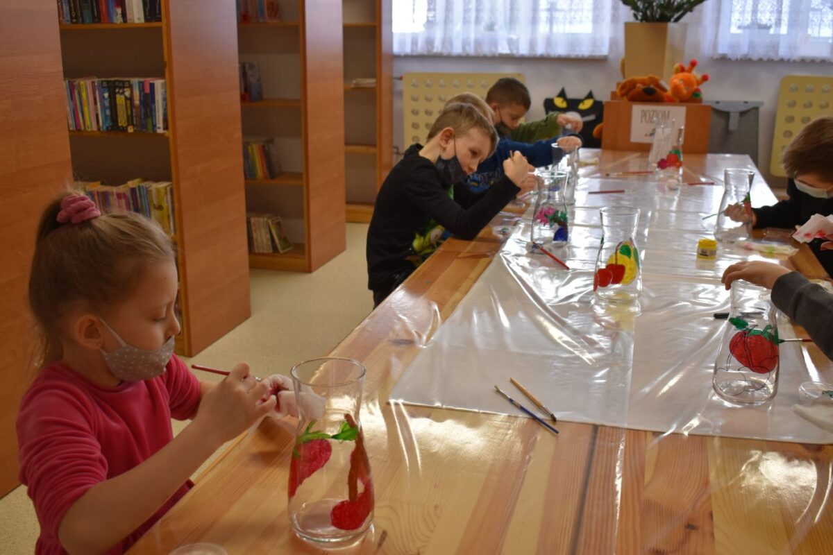 W bibliotece grupka dzieci z kolorowymi noskami za nimi regały z książkami