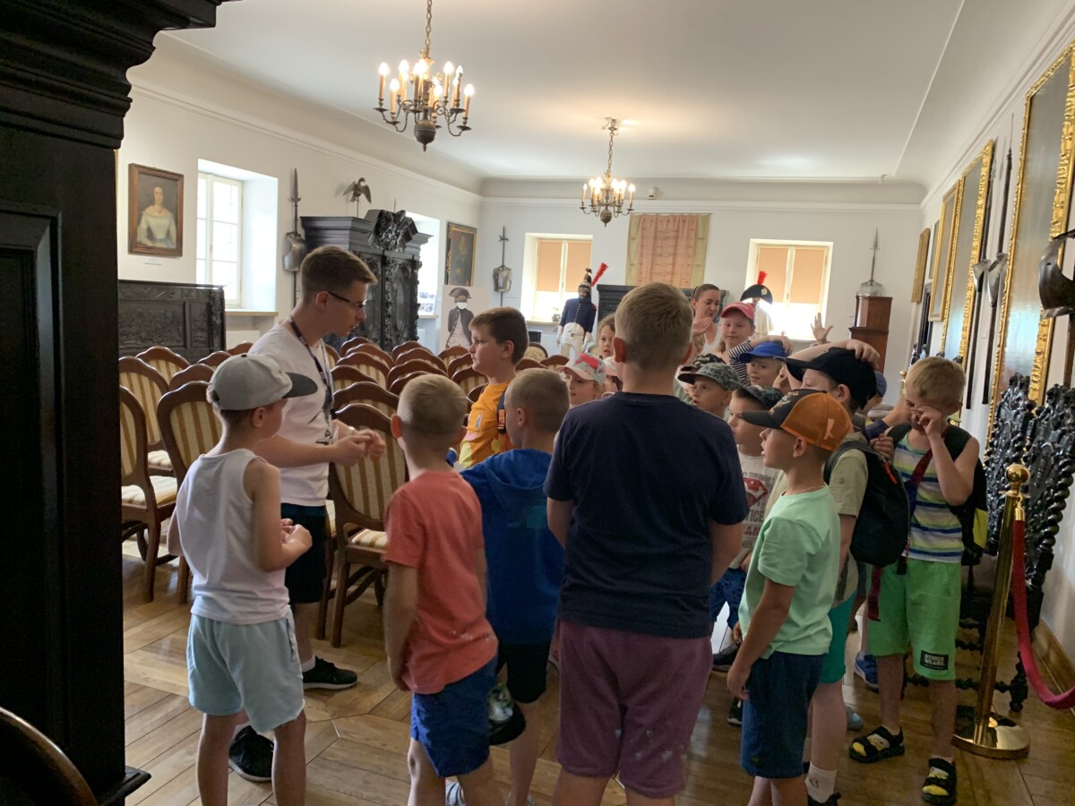 W sali muzealnej dzieci słuchają przewodnika, który im opowiada.