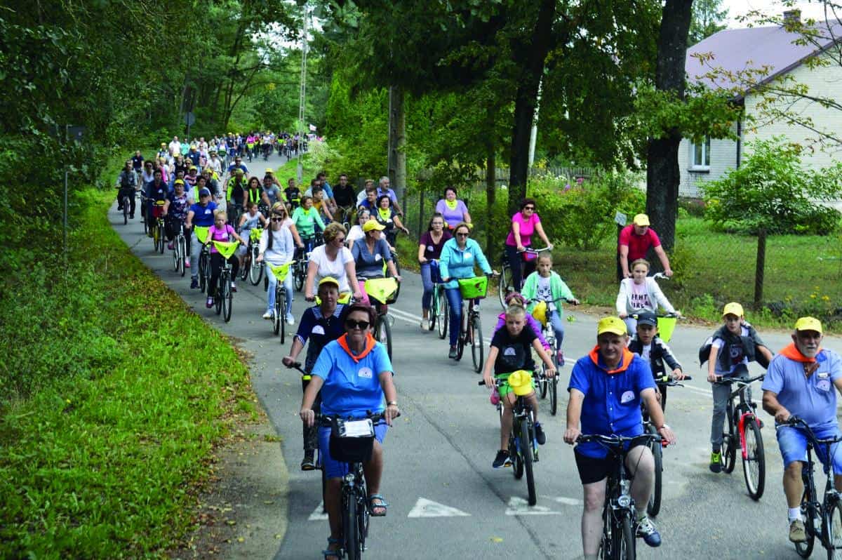 Uczestnicy rajdu rowerowego jadący ulicą. w żółtych czapkach ichustach w kolorze pomarańczowym