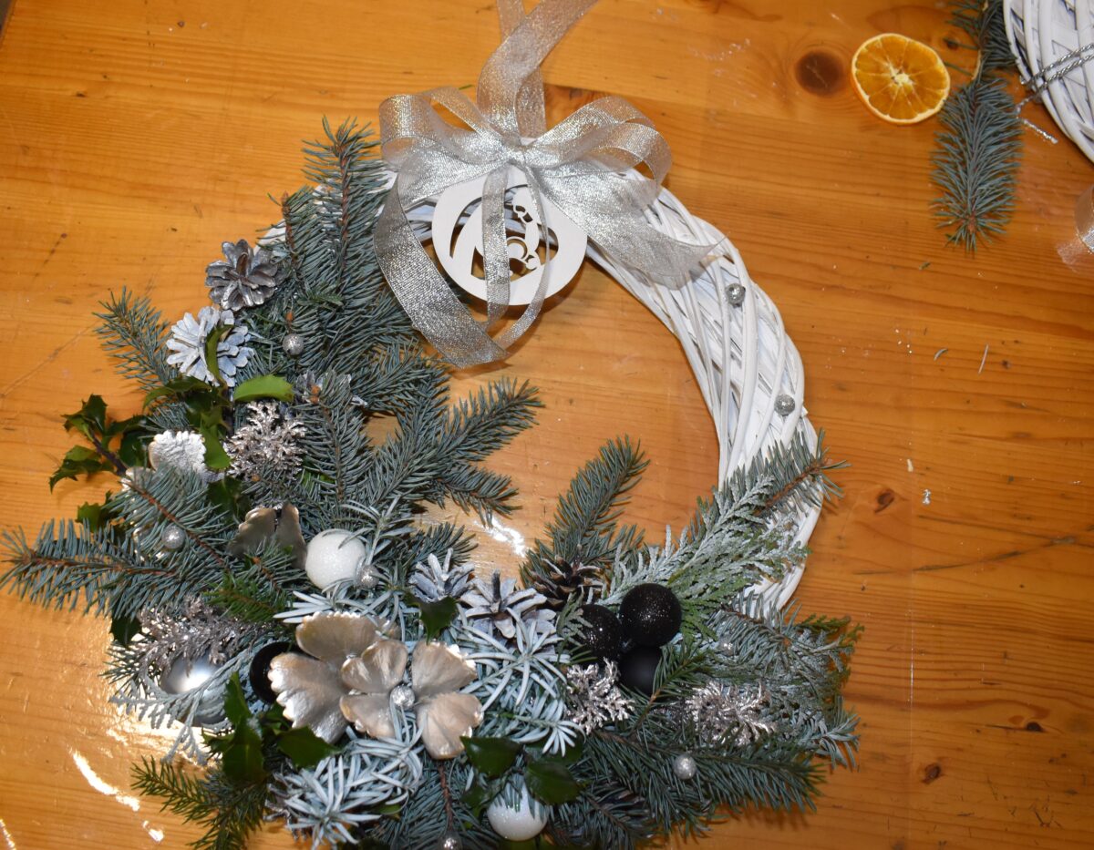 422 Biały pleciony wianek z dużą ilością gałązek świerku, złotymi bombkami i kokardą.