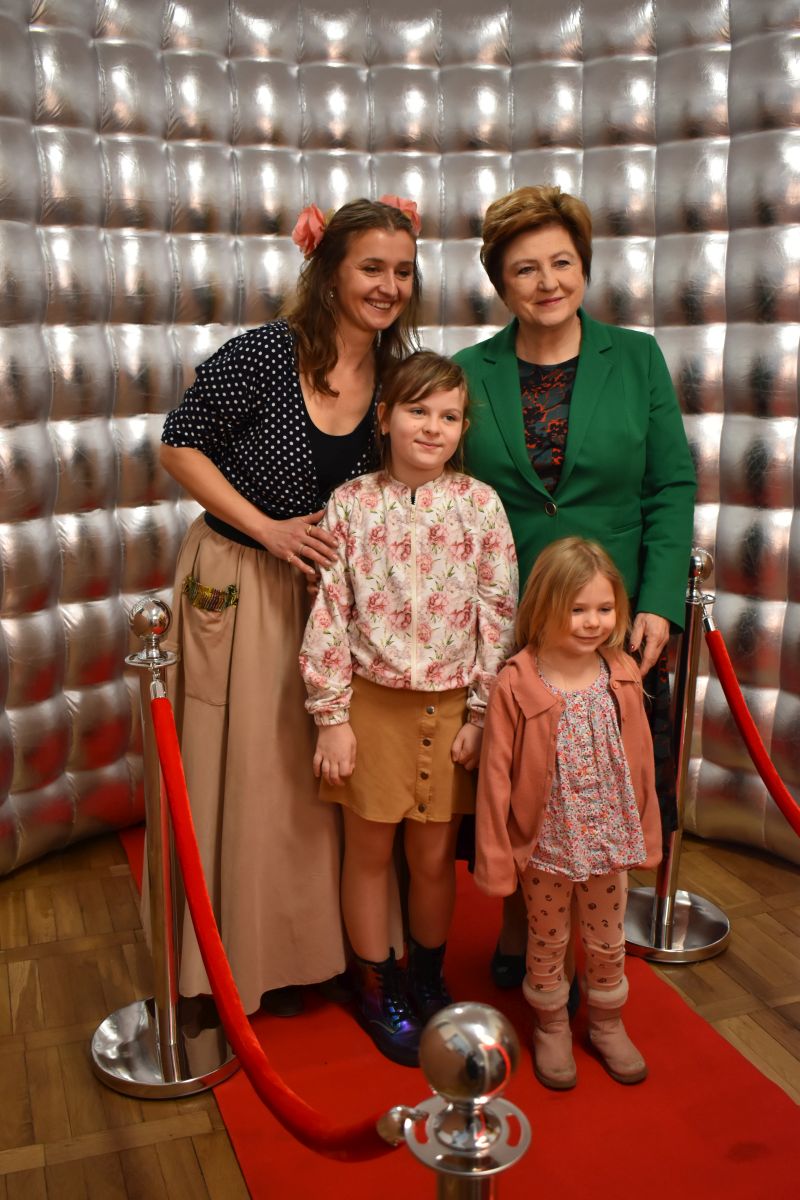 Na obrazku trzy kobiety i dziecko na czerwonym dywanie. Wszyscy są elegancko ubrani, co do zasady, że mogą brać udział w prestiżowych wydarzeniach lub galii.