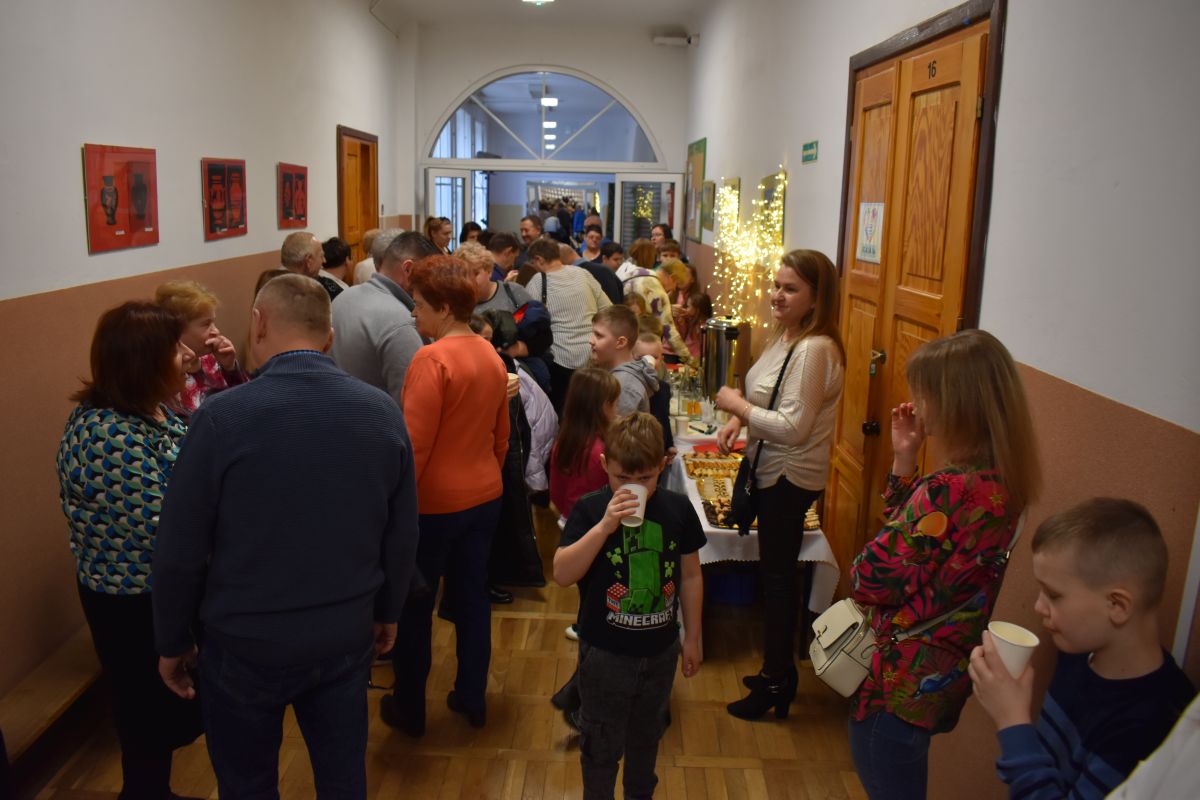 Na udostępnienie jest grupa ludzi, która stoi w przerwie i szerokim korytarzu. Osoby te mają sobie różne ubrania i wyglądają na to, że są w trakcie rozmów lub oczekiwania na coś.