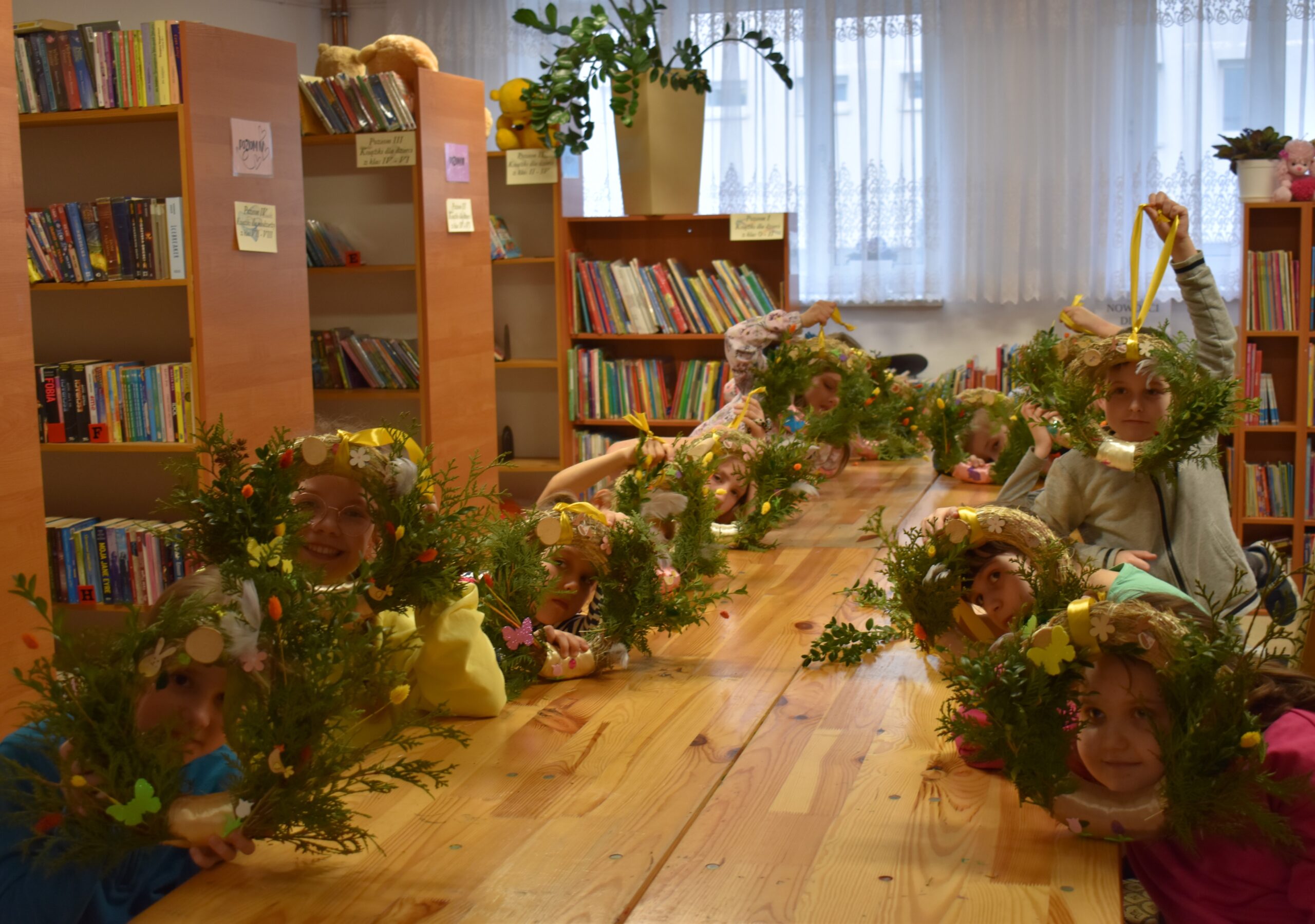 Na obrazku widać dzieci noszące korony z kwiatami, które siedzą przy kradzieży w bibliotece. Wyglądają na zaangażowane i zadowolone, a następnie przedstawiają książkę dotyczącą przestrzegania zasad nauki lub naukowej zabawy.