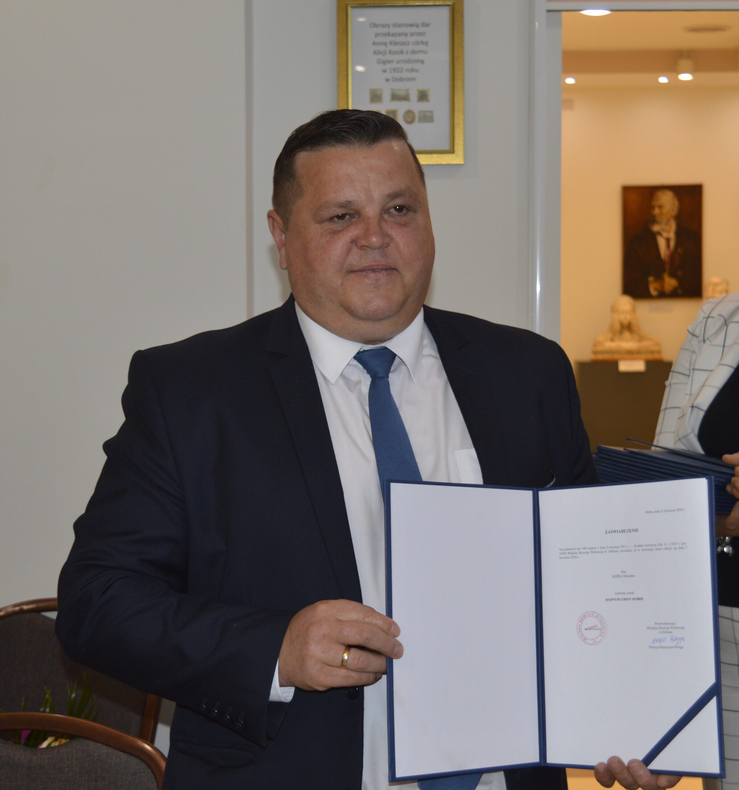Na obrazku mężczyzn w garniturze, który trzyma otwarty segregator z dokumentami. Stał na szczeblu biurowym otoczenia.