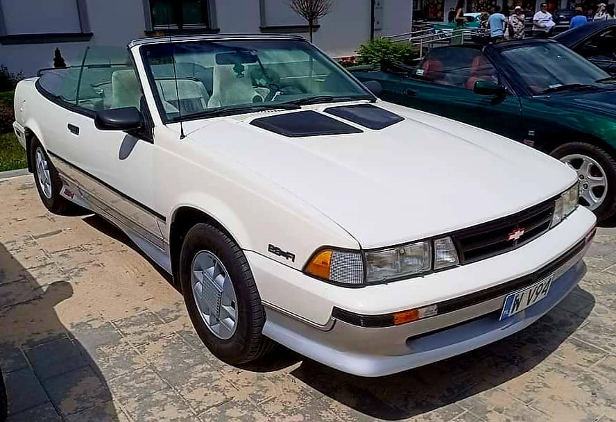 Na miejscu pojawia się biały Chevrolet Cavalier Z24 kabriolet ukryty na utwardzonej nawierzchni. Samochód ma czarny, składany dach oraz konstrukcję aerodynamiczną z charakterystycznymi otworami wentylacyjnymi na masce.