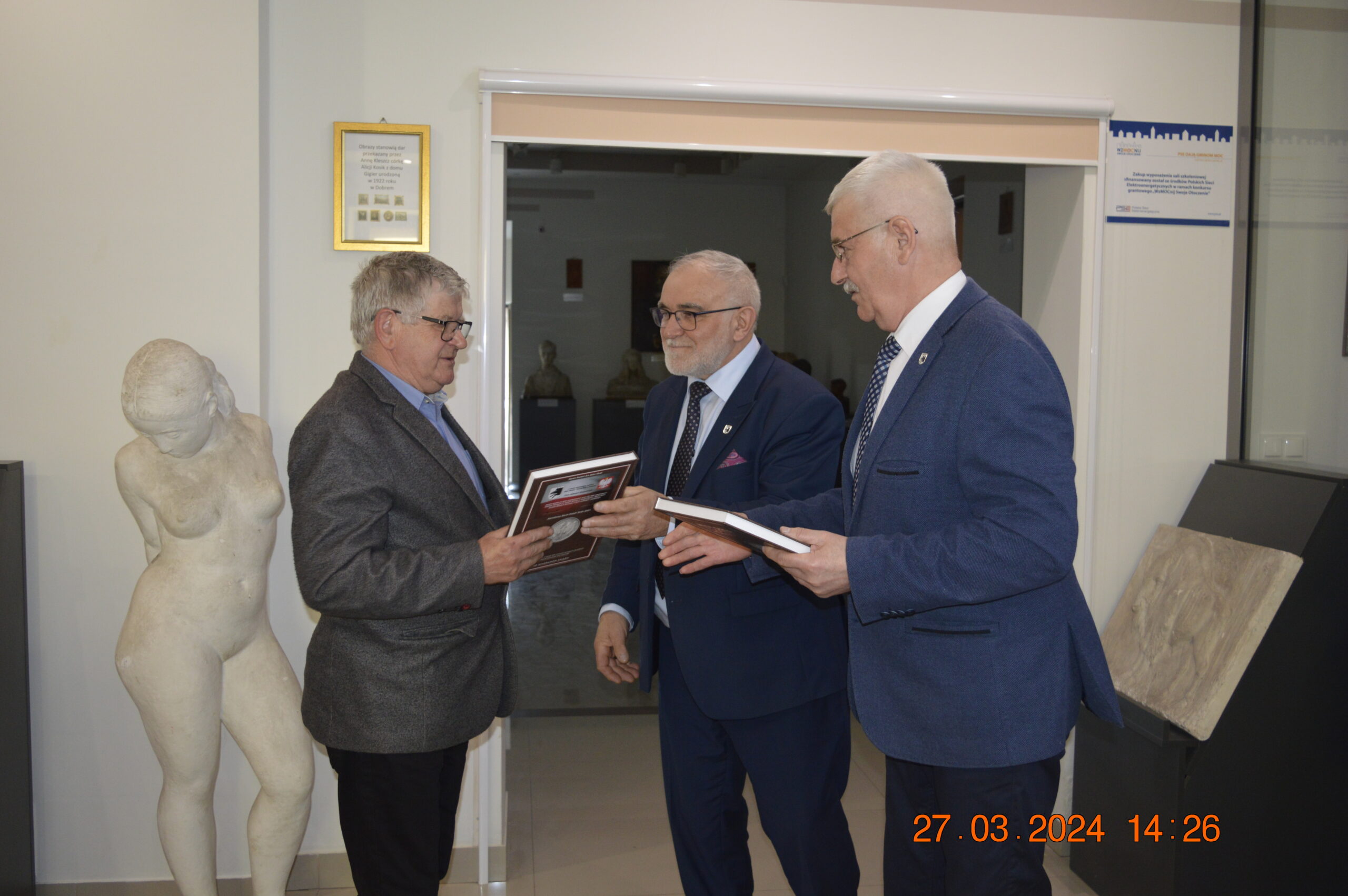 Na obrazach trzech starszych mężczyzn w garniturach wymienianych się dokumentami w dodatkowych klasycznych rzeźbach i certyfikatach na ścianach. Jeden z nich, drugiemu plakietkę, podczas gdy drugie ich z boku.
