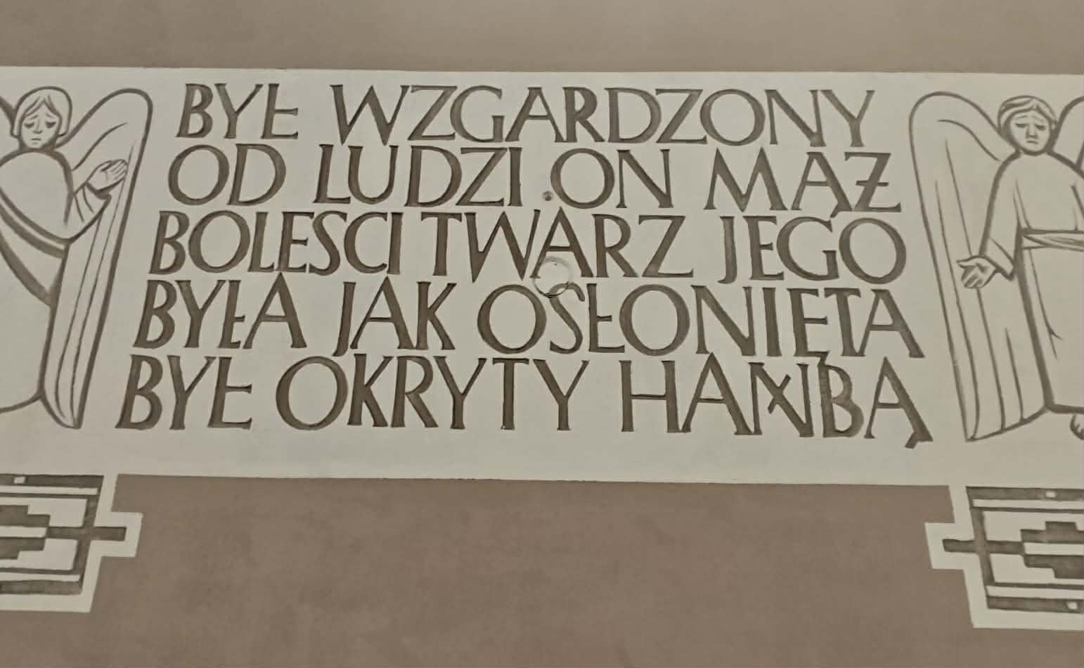 Na beżowym tle widnieje tekst z religijnym przesłaniem. Towarzyszą mu dwa stylizowane wizerunki aniołów. Kolory są stonowane, a litery są ciemnobrązowe.