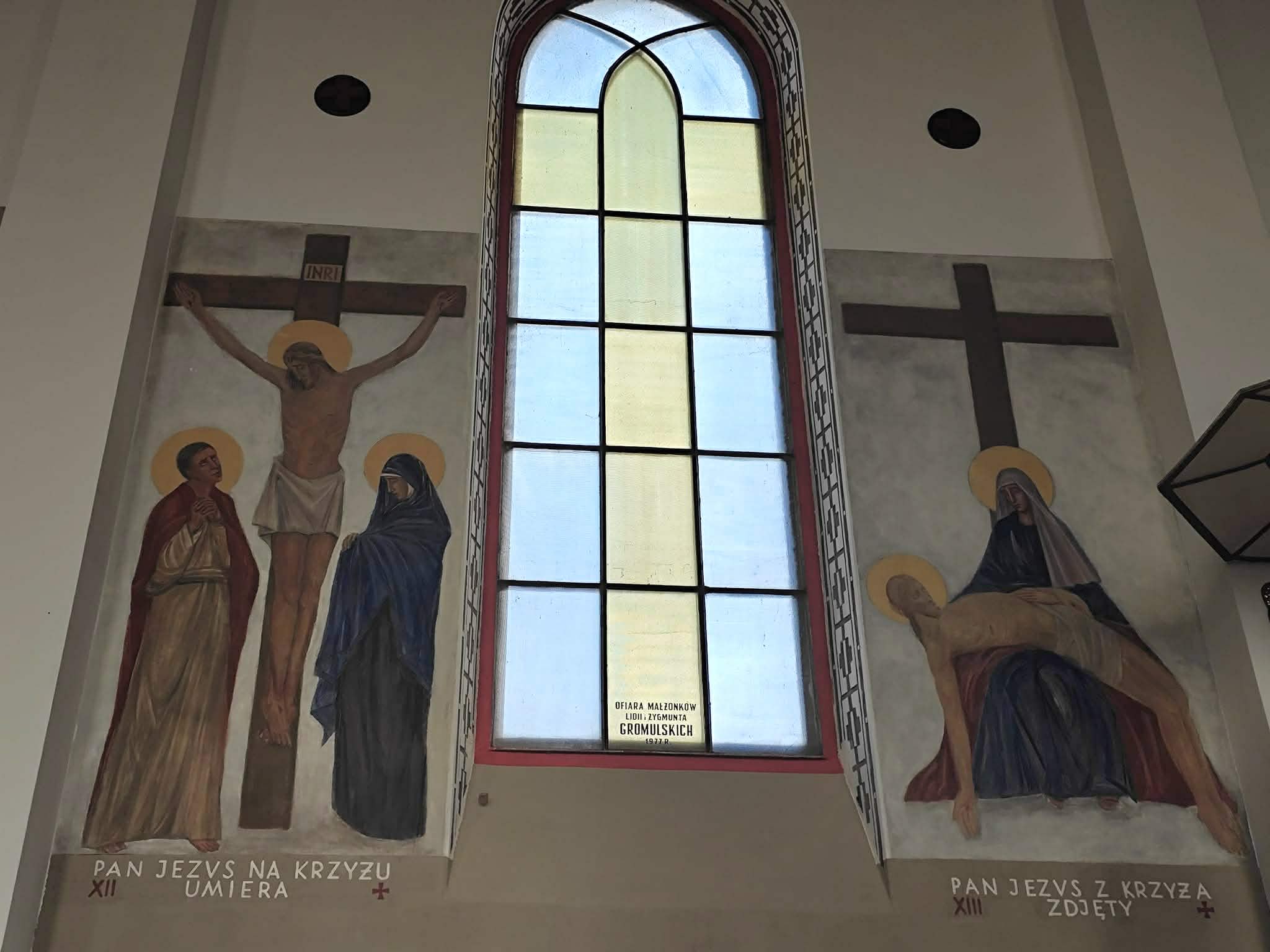 Na obrazie Jezus na krzyżu i scena zdjęcia z krzyża. Kolory dominujące to brązowy i niebieski. Tło to duże okno z witrażem.