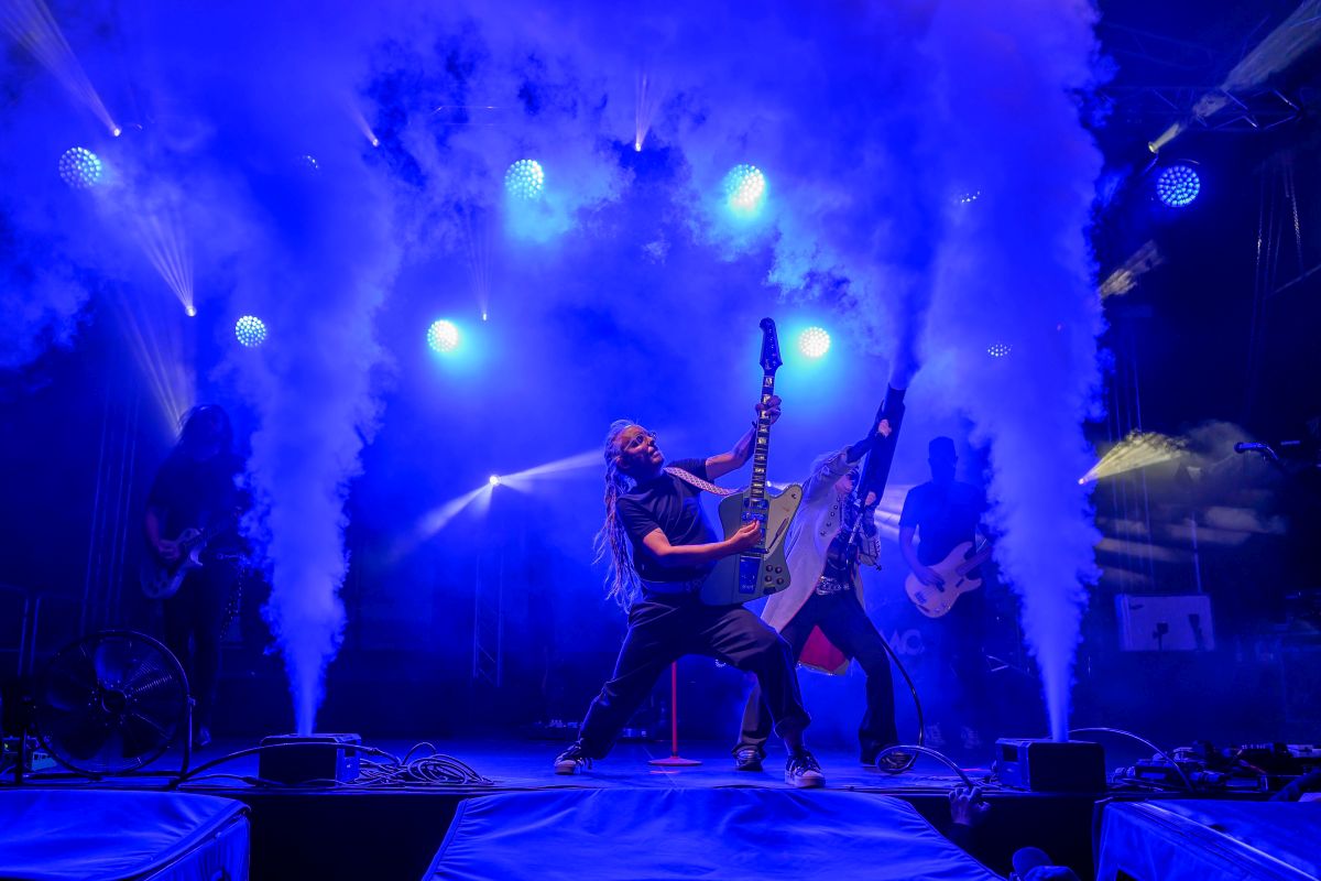 Koncert rockowy z zespołem na scenie, dynamiczne światła w niebieskich tonach, efekty dymu w tle.